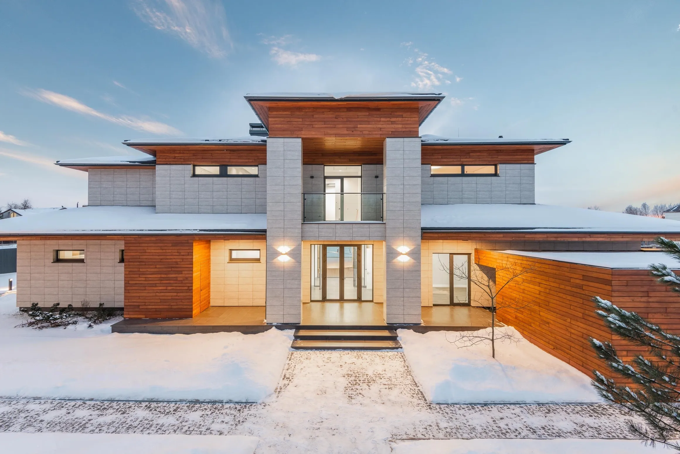 Modern two-story house with wood accents and large windows in snowy setting.